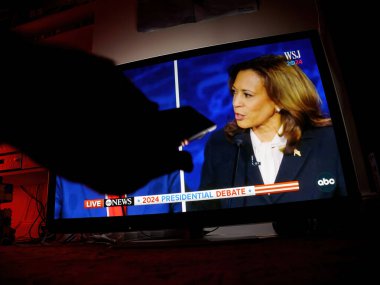 Paris, Fransa - 11 Eylül 2024: Kamala Harris ve Donald Trump arasında başkanlık tartışmasını gösteren bir TV ile oturma odası sahnesi, ön planda ise bir erkeğin uzaktan kumandası var.