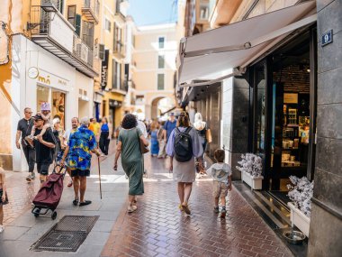Palma, İspanya - 8 Temmuz 2024: Palma de Mallorca 'da dükkanın önünden geçen yerli halk ve turistlerin bulunduğu hareketli bir sokak keşfeden anne ve oğlu. Canlı şehir sahnesinde insanlar alışveriş yapıyor.
