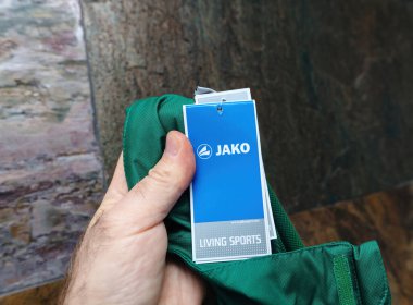 Berlin, Almanya - 3 Nisan 2024: Jako Yaşayan Spor Giysileri etiketini açan bir erkek el, marka ve fiyat bilgisini ortaya koyuyor