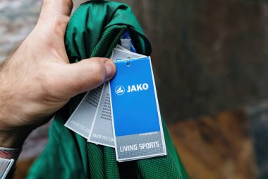 Berlin, Almanya - 3 Nisan 2024: Jako Living Sportswear 'in boks boksunu açan bir erkek el, taştan bir arka planda etiketi gösteriyor, spor kıyafetlerinin markasını vurguluyor