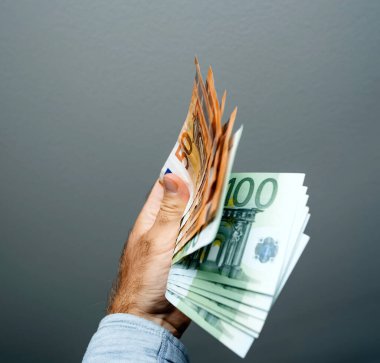 Bir erkek el, servet ve kolay para kavramını temsil eden, gri bir arkaplan üzerine kurulmuş, bir fan gibi birden fazla euro banknotları tutuyor.