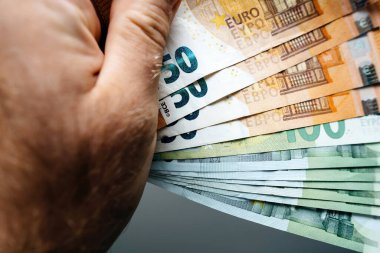 Zenginlik ve kolay para kavramını temsil eden ve refahı vurgulayan birden fazla avro banknotunu elinde tutan bir erkek el