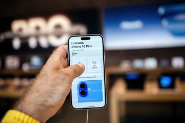 Paris, Fransa - 20 Sep 2024: En son iPhone 16 Plus akıllı telefonu bir Apple mağazasında, arka planda dağıtılmış tanıtım afişleriyle birlikte elinde tutuyor