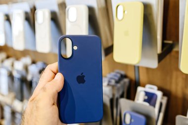 Paris, Fransa - 20 Eylül 2024: Bir Apple mağazasında, arka planda birden fazla kasa bulunan iPhone 16 için mavi silikon çanta tutan erkek el