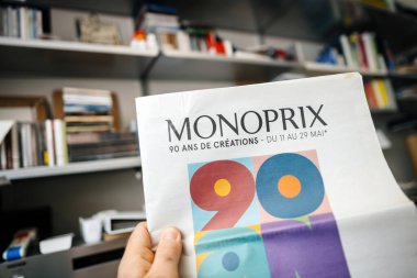 Paris, Fransa - 21 Şubat 2024: Monoprixler 'in 90. yıldönümü için özel indirimli ticari bir gazete ilanı tutan erkek el, arka planda raflarda yakalandı