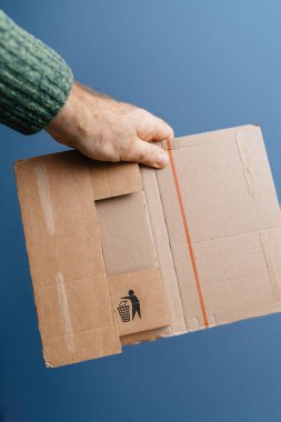 Close-up of a persons hand holding a cardboard box with a recycling symbol, emphasizing waste management, eco-friendly practices, and sustainability against a blue background clipart