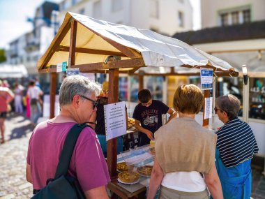 Hardelot, Fransa - 20 Ağustos 2023: Hardelot, Fransa 'da açık hava gıda piyasası sahnesi, güneşli bir günde insanların ahşap tezgahlara göz atması ve fırınlanmış ürünler satması.