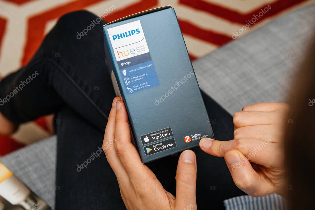 Paris, France - Aug 16, 2024: A woman points to the Zigbee certified product text on the Philips Hue package containing the smart bridge device for smart lighting
