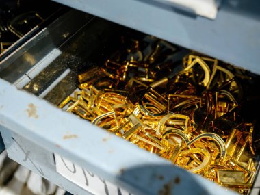 A drawer filled with shiny gold buckles, used for leather crafting, showcasing the tools and hardware involved in producing belts, bags, and accessories. clipart