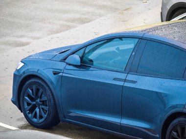 Neufchatel-Hardelot, Fransa - 18 Ağustos 2023: Yağmurlu bir günde, parlak tasarımı ve modern özelliklerini sergileyen mavi bir Tesla elektrikli aracı ıslak bir yüzeye park edilmiştir.