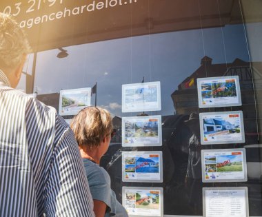 Neufchatel-Hardelot, Fransa - 20 Ağustos 2024: Bir çift, Fransa 'nın Hardelot kentindeki bir vitrindeki gayrimenkul ilanlarını inceleyerek, sergilenen ve satışa sunulan mülkleri inceliyor