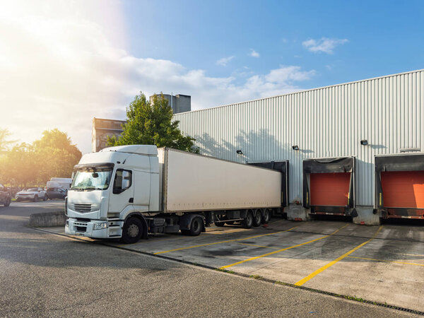 A white truck is parked at a warehouse loading dock, ready for freight handling, showcasing a commercial shipping and logistics operation