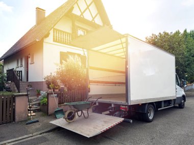 Açık rampası, el arabası ve araç gereçleri olan bir kamyoneti bir banliyö evinin önünde yüklemeye ya da boşaltmaya hazır halde taşımak.