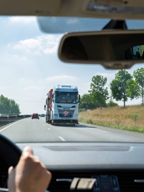 Paris, France - Aug 17, 2023: Point of view from inside a car on the highway, approaching a DAF truck transporter carrying multiple trucks, surrounded by clear skies and roadside greenery clipart