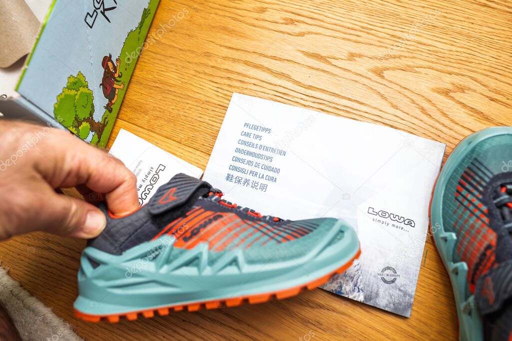 Paris, France - Apr 13, 2024: LOWA kids hiking shoe with a colorful design sits beside a care guide on a wooden surface, part of the unboxing process for outdoor footwear