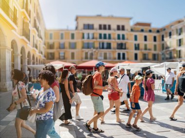 Palma, İspanya - 8 Temmuz 2024: İspanya 'nın Mallorca kentindeki canlı Plaza Belediye Başkanı' nda renkli tarihi binalar, pazar yerleri ve arka planda parlak yaz güneşiyle yürüyen bir grup turist