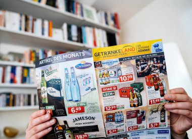 Frankfurt, Almanya - 3 Kasım 2023: Alman meşrubat kataloğu okuyan ve Vitsoe raflarının arka planda kitaplarla dolu olduğu renkli içecek terfileri ile Getrankeland