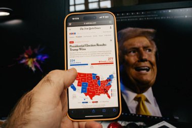 Paris, Fransa - 6 Kasım 2024: Bir akıllı telefon New York Times 2024 başkanlık seçim sonuçlarını gösteriyor ki Trump Harris 'i yenerken arka planda ABD seçim haritası var
