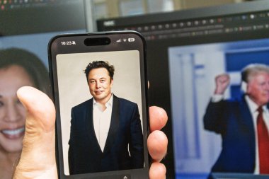 Paris, Fransa - 6 Kasım 2024: Bir akıllı telefon, Elon Musk 'un bir portresini, Kamala Harris ve Donald Trump' ın ayrı monitörlerde görüntülerinin yer aldığı bir arka planda sergiliyor
