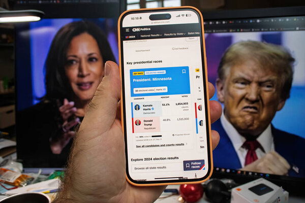 Paris, France - Nov 6, 2024: A smartphone shows CNN s 2024 election results for Minnesota, with Kamala Harris leading Trump, and images of Harris and Trump in the background