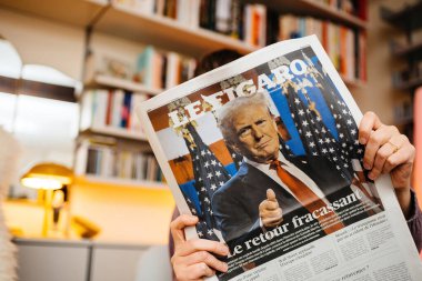 Paris, Fransa - 7 Kasım 2024: Samimi bir oturma odasında Fransız Le Figaro gazetesi okuyan kişi, Donald Trump 'ın ABD politikasına etkili dönüşünün ön sayfasında yer alıyor.