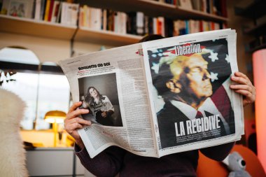 Paris, France - Nov 7, 2024: Woman reading French newspaper Liberation in a cozy living room, featuring front-page headline La Recidive on Donald Trump s political comeback in the U.S. clipart