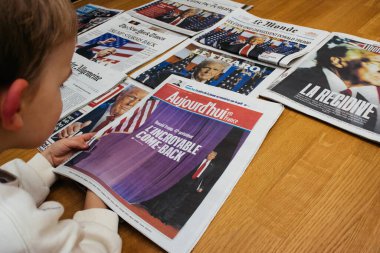 Paris, Fransa - 7 Kasım 2024: Tahta bir masada uluslararası gazetelere bakan meraklı çocuk, her biri Donald Trump 'ın siyasi dönüşüyle ilgili manşetlerde, dünya haberlerine erken ilgi gösteriyor