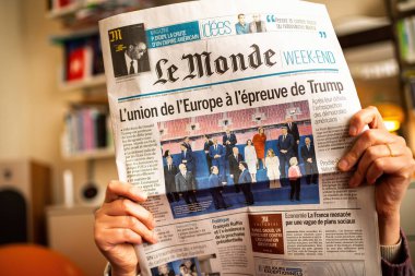 Paris, France - Nov 13, 2024: Le Monde newspaper headline on European unity in response to Trump, held by a woman reading indoors, emphasizing political challenges and alliances clipart