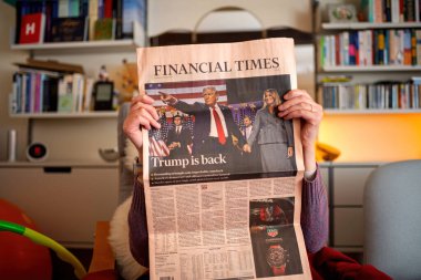 Paris, Fransa - 13 Kasım 2024: Oturma odasında Financial Times 'ı okuyan bir kadın Trump geri döndü, uluslararası haberlerde Trump, eşi Melania ve oğlunun yer aldığı