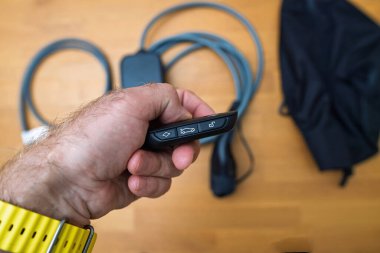 Bir el, arka planda elektrik kablosu ve adaptörü olan ve modern EV teknolojisini sembolize eden bir arabanın anahtarlığını tutuyor.