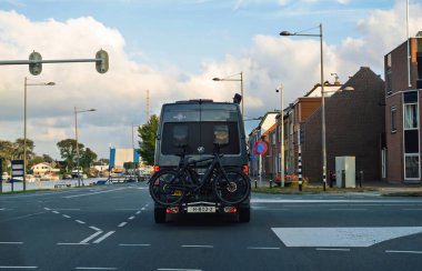 Texel, Hollanda - 29 Ağustos 2024: Arkasına iki bisiklet monte edilmiş bir Volkswagen karavan Hollanda 'da manzaralı bir kanal ve arka planda binalar bulunan bir kasabadan geçerken görüldü.
