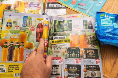 Frankfurt, Germany - Aug 22, 2024: Hand pointing at a German beverage flyer featuring soft drinks, juices, and beers, with discounts and promotional offers highlighted in a colorful layout clipart