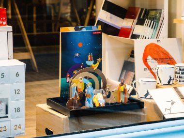 Baden-Baden, Almanya - 29 Kasım 2924: Konforlu bir dükkanda sanatsal fincanlar, takvimler ve kırtasiyelerin yanı sıra canlı bir modern doğum sahnesinin yer aldığı yaratıcı bir vitrin.