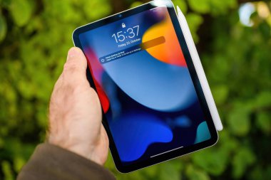 Paris, Fransa - 21 Ekim 2021: Elma kalemli iPad Mini 'yi tutan bir el, açık alanda bulanık yeşil bir arka plana karşı canlı bir ekran sergiliyor.