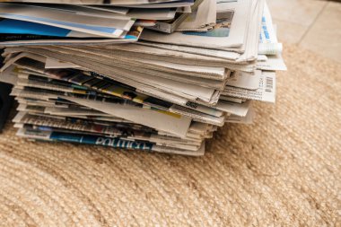 Bej bir halıya yerleştirilmiş bir yığın karışık gazete. Medya çeşitliliği, küresel haberler ve günlük ev ortamında basılı gazetecilik geleneği.