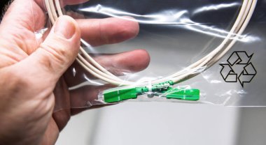 Yeşil konnektörlü fiber optik kabloyu yakın plan, yüzeyinde geri dönüşüm sembolü olan şeffaf bir plastik torba içinde sergileniyor.