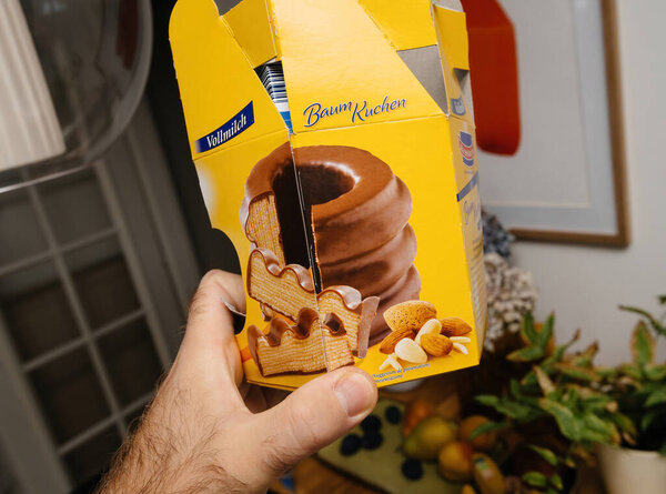 Paris, France - Oct 21, 2021: Hand holding a vibrant yellow Vollmilch Baumkuchen box showcasing the layered cake design with chocolate coating