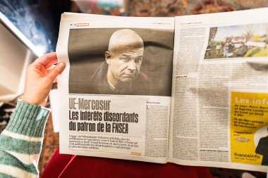 Paris, France - Dec 9, 2024: Person reading a Liberation article discussing the conflicting interests of FNSEA leader regarding the EU-Mercosur trade deal and its impact on agriculture clipart