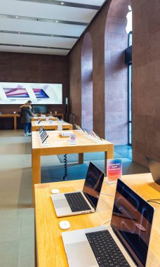Paris, Fransa - 10 Aralık 2024: Modern bir ortamda parlak ışık altında ahşap masalarda MacBooks, iPad 'ler ve aksesuarların yer aldığı bir Apple mağazasının dikey çekimi.