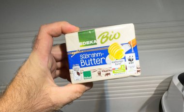 Berlin, Germany - Nov 22, 2024: A hand holding Edeka Bio Sussrahm Butter package featuring premium quality and organic certification labels, highlighted against a neutral background. clipart