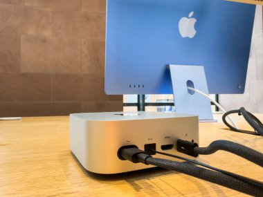 Paris, Fransa - 10 Aralık 2024: Bir Apple mağazasında sergilenen ve arka planda mavi bir iMac eşleştirilmiş M4 bağlantılı yeni bir Mac Mini ve Thunderbolt kablosu.