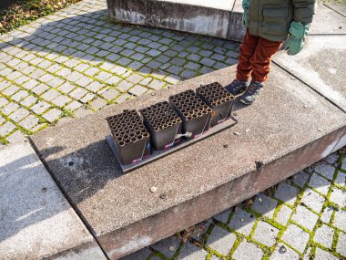 Strasbourg, France - Jan 1, 2025: A setup of fireworks canisters placed on a concrete bench in the Port du Rhin neighborhood, with a child nearby, symbolizing post-New Year celebrations. clipart