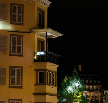 Strazburg 'daki Kleber Oteli' nin gece görüşü. Işıklı tabelalı ve pencereli. Bir ağaç ve çevreleyen mimari büyüleyici atmosfere katkı sağlar..