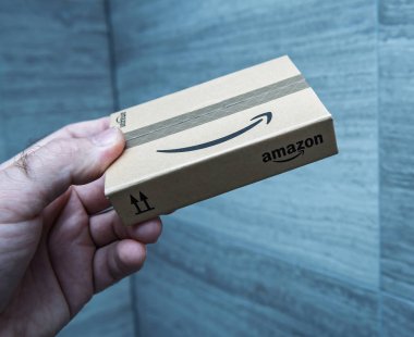 Paris, Fransa - 21 Kasım 2021: Amazon markalı şık bir karton paket, lojistik ve depo verimliliğini sembolize eden desenli endüstriyel bir arka plana karşı hazırlandı.