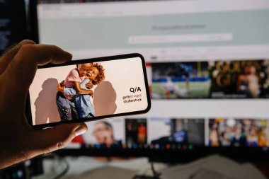 Paris, Fransa - 7 Ocak 2025: Q ve A Getty Images Shutterstock etiketli bir resim gösteren akıllı telefon, Getty Images web sitesinin işbirliğini sembolize eden bir bilgisayar ekranının önünde tutuluyor.