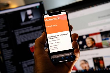 Paris, Fransa - 7 Ocak 2025: Shutterstock ve Getty birleşme duyurusunun etkinlik detaylarını gösteren bir akıllı telefon ekranı, ilgili içeriği gösteren bilgisayar monitörleri önünde düzenlendi.