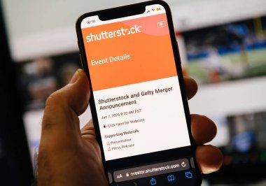 Paris, Fransa - 7 Ocak 2025: Shutterstock ve Getty birleşme duyurusunun medyayla ilgili görsellere sahip bilgisayar monitörleri karşısında görüntülendiği akıllı telefonun yakın çekimi.