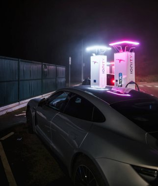 Lyon, Fransa - 1 Ocak 2025: Ionity istasyonunda loş bir çevrede parlak pembe ve beyaz şarjlı Porsche elektrikli araba şarj ediliyor.