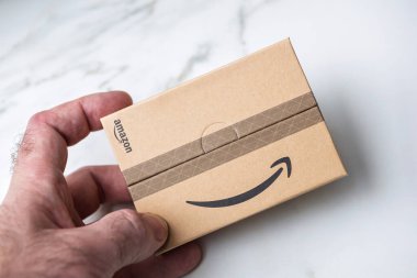 Paris, Fransa - 22 Kasım 2021: Eline tutulan, mermer arka plana yaslanmış, basit ve güvenli ambalaj sergilenen, imzalı karton Amazon paketi