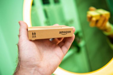 Paris, France - Nov 22, 2021: Close-up of a small Amazon package held in a hand against a vibrant green background, showcasing minimalist branding and eco-friendly packaging. clipart